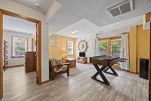 A spacious living area with a foosball table, wooden furniture, and a large window with curtains.