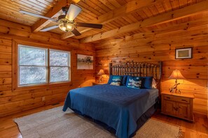 Une chambre dans une cabane en bois, avec un lit, des tables de chevet, un ventilateur de plafond et une fenêtre.