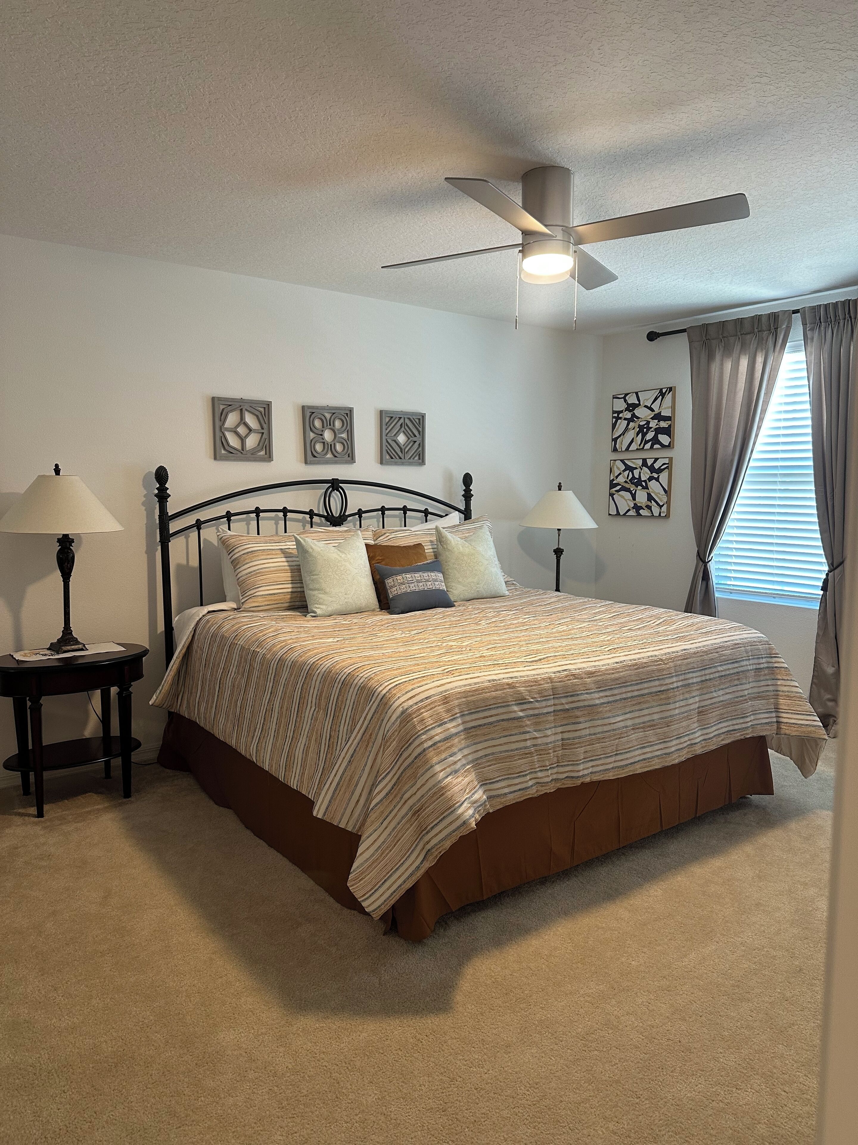 A bedroom with a bed, two nightstands, a ceiling fan, and artwork on the walls.