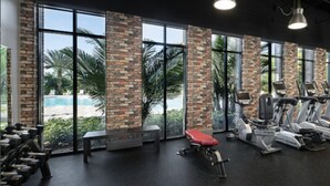 Ett gym med träningsutrustning, stora fönster och utsikt över en pool.