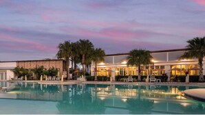 A pool area with lounge chairs and umbrellas, a building with a stone facade, and palm trees. - Fantastic Townhouse Champions Gate! (Davenport)