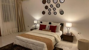 A bedroom with a bed, bedside tables, a wall-mounted mirror, and a rug. - Cozy 3BR home - gated estate - Tema - top security (Tema)