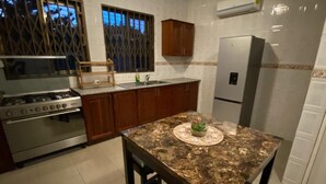 A kitchen with a granite countertop, stainless steel appliances, wooden cabinets, and a window with bars. - Cozy 3BR home - gated estate - Tema - top security (Tema)