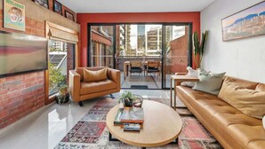 A modern living room with a leather sofa, a coffee table, and a dining area with a glass door leading to an outdoor space.