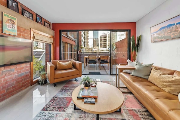 A modern living room with a leather sofa, a coffee table, and a dining area with a glass door leading to an outdoor space.