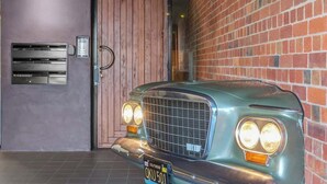 A vintage car parked in a garage with a brick wall and a wooden door.