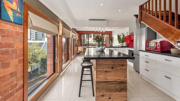 A modern kitchen with a large island, white cabinetry, and a wooden staircase.