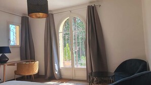 Une pièce comprenant un lit, un bureau, une chaise, une lampe et une fenêtre avec des rideaux.