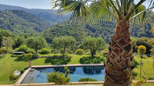 Une piscine offrant une vue sur un jardin luxuriant et sur des collines lointaines.