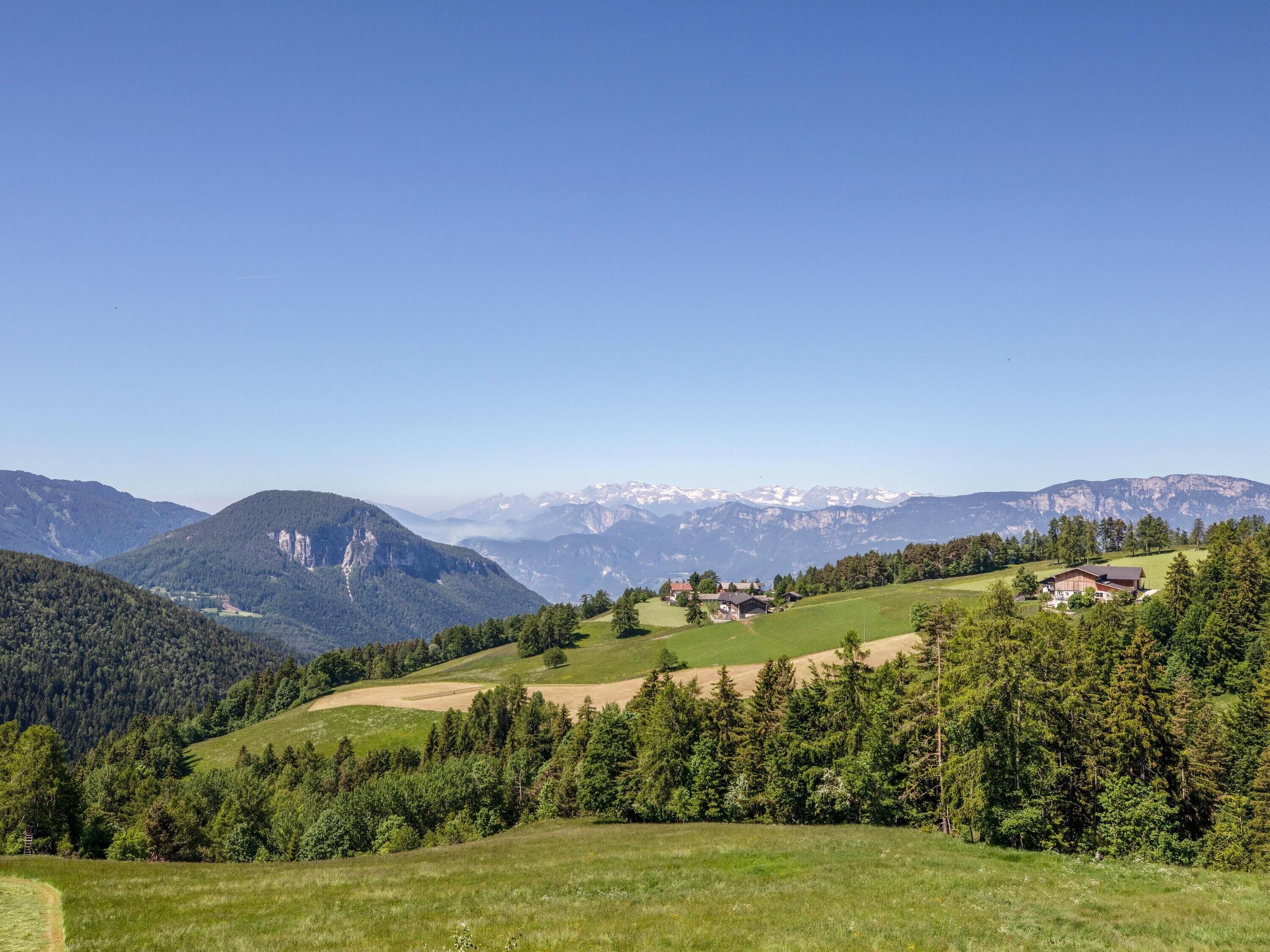 A rural landscape with rolling hills, a small house, and distant snow-capped mountains under a clear sky.