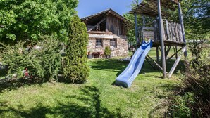 Una casa de madera rústica con base de piedra, una estructura de juegos de madera con tobogán y un césped bien cuidado.