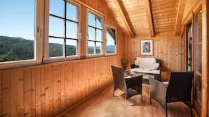 Ein Zimmer mit Holzwänden, einem Tisch und Stühlen, großen Fenstern und einem gerahmten Bild an der Wand.