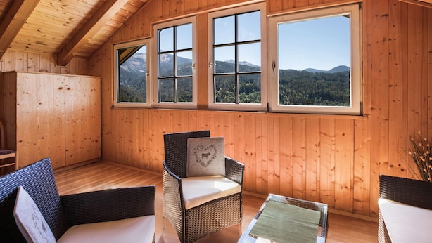 Eine Holzhütte mit drei großen Fenstern, Korbmöbeln und Blick auf die Berge.