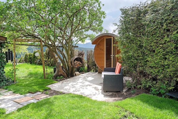 A cozy outdoor seating area with a wooden pergola, a circular wooden structure, and a stone pathway.