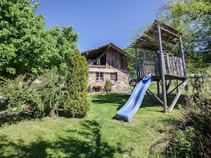 A rustic wooden house with a stone foundation, a wooden deck, and a blue slide.