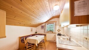 Et hyggeligt køkken med træloft, et spiseområde med bord og bænk, og et vindue med udsigt.