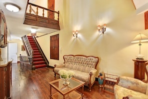 Une pièce avec un escalier en bois, un canapé, une table basse surmontée d’un vase et une lampe.