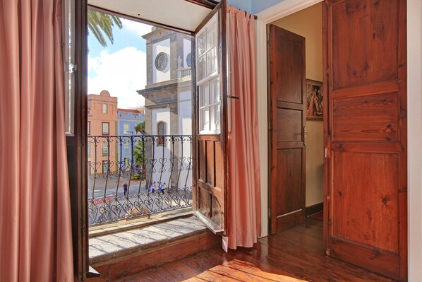 A room with a wooden floor, a window with a view of buildings, and a door.