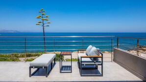 Un balcón con vista al océano, dos sillones de descanso, una mesita y una planta.