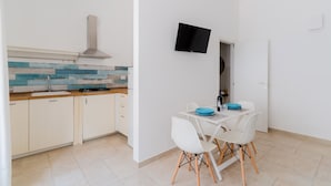 A modern kitchen with white cabinets, a blue and white backsplash, a stainless steel range hood, and a dining area with white chairs and a blue bowl.