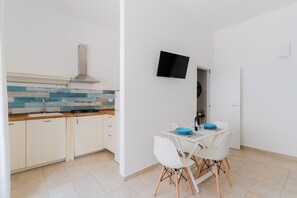 Una cucina moderna con mobili bianchi, zoccolo blu e bianco, cappa aspirante in acciaio inossidabile e un'area pranzo con sedie bianche e una ciotola blu.
