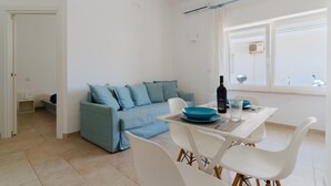A modern living room with a sofa, dining table, chairs, and a window with an air conditioning unit.