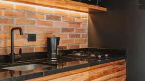 A kitchen with wooden cabinetry, a brick backsplash, a black countertop, a stainless steel sink, a coffee maker, and a microwave. - Industrial Chic Loft in Front of Unicentro Mall (Medellín)
