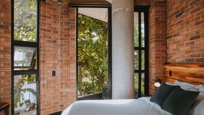 A bedroom with a brick wall, a large window, and a bed with white bedding. - Industrial Chic Loft in Front of Unicentro Mall (Medellín)