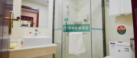 Un baño de hotel con ducha de vidrio, lavamanos y inodoro.