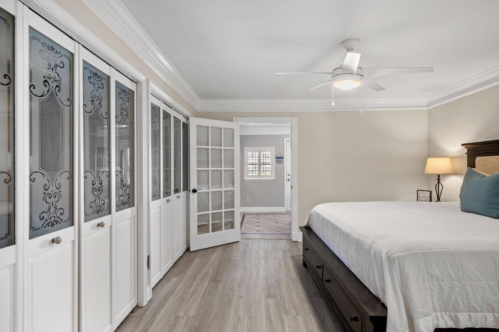 A bedroom with a bed, a nightstand, a lamp, a ceiling fan, and a walk-in closet with glass doors.