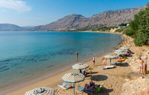 Une plage avec une eau d’un bleu limpide, des parasols et des gens qui prennent un bain de soleil.