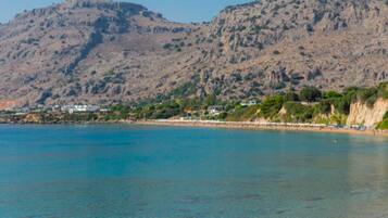 A coastal landscape with a clear blue sea, rocky cliffs, and a beach with buildings along the shore.