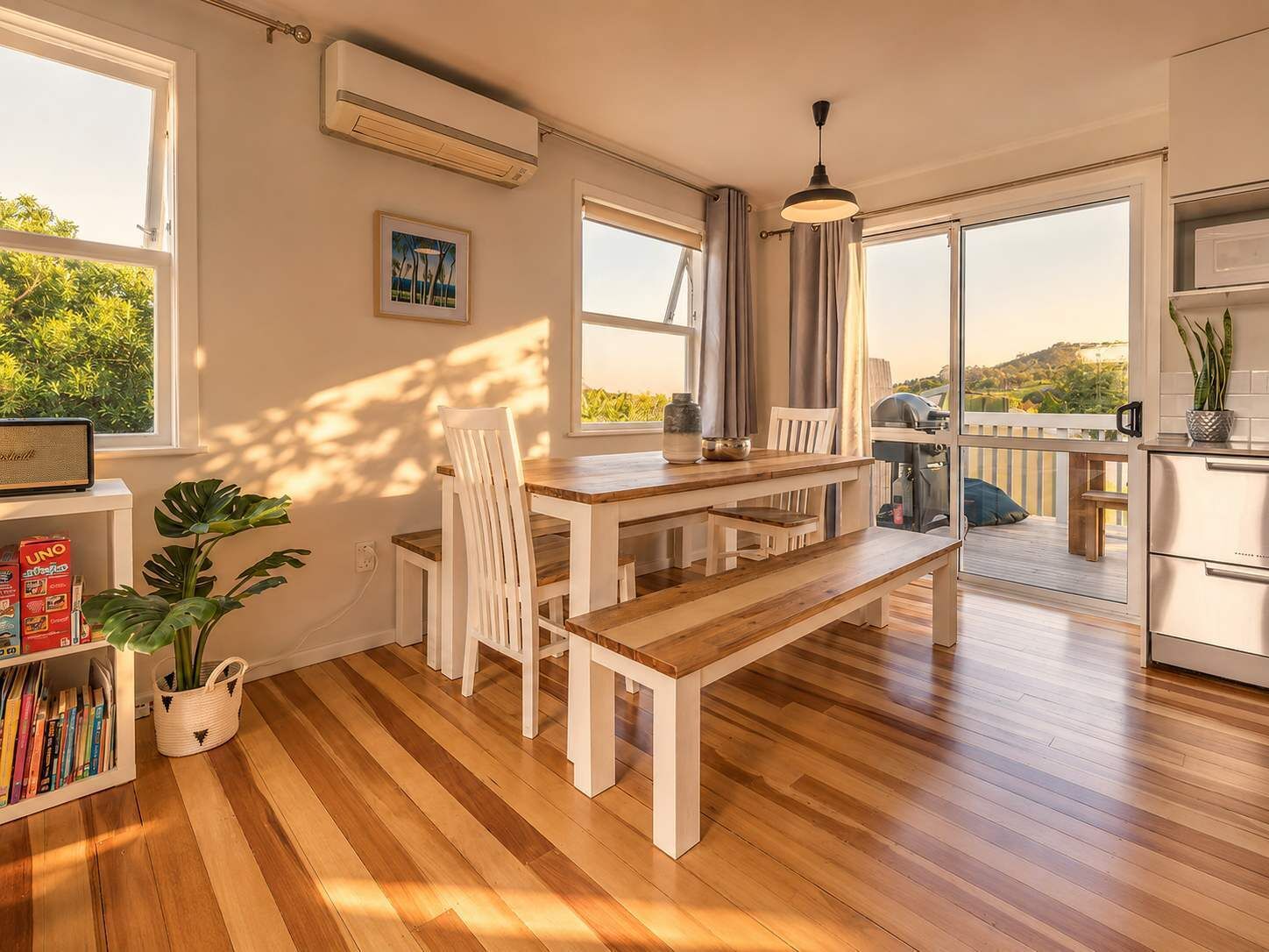 A modern kitchen with a wooden table and chairs, a hanging light fixture, and a view of the outdoors.