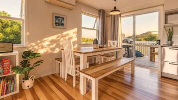 A modern kitchen with a wooden table and chairs, a hanging light fixture, and a view of the outdoors.