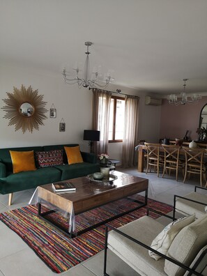 A living room with a green sofa, a wooden coffee table, a colorful rug, and a dining area with wooden chairs and a table.