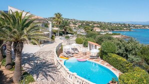 A pool area with a clear view of the sea, surrounded by palm trees and a stone pathway.