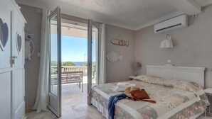 A bedroom with a bed, a bench outside, and a view of the beach.