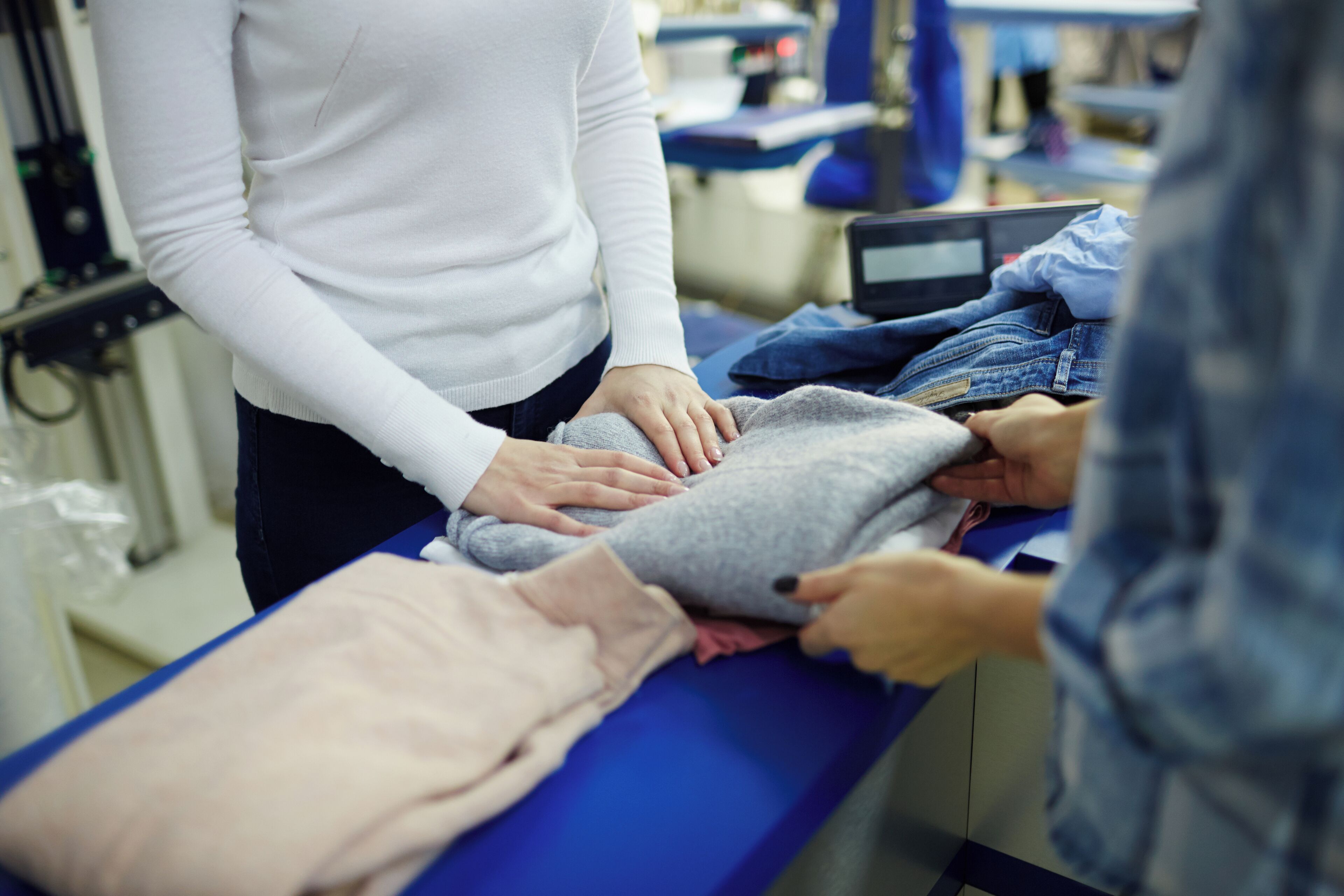 A person in a white top and dark pants standing at a blue table with various clothing items.