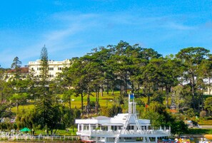 Un barco blanco con una estructura blanca en la parte superior, rodeado de follaje y un edificio al fondo.