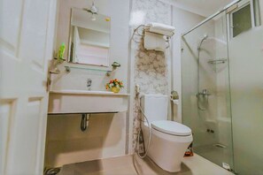 Un baño moderno con cabina de ducha de vidrio, inodoro, lavamanos con espejo y un pequeño arreglo floral en la encimera.