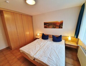 Quarto de hotel com cama, guarda-roupa, mesa de cabeceira, abajur e um quadro na parede.