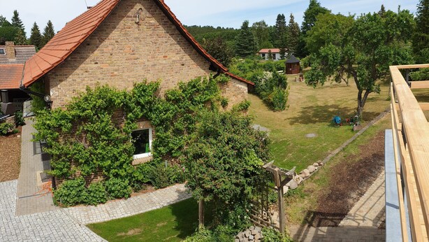 A stone building with a red roof, surrounded by a well-maintained garden and a paved pathway. - Vacation apartment 1 - Ferienhof Rätzsee (Wustrow)