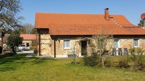 A two-story stone house with a red-tiled roof, a visible chimney, and a small front porch with outdoor seating. - Vacation apartment 1 - Ferienhof Rätzsee (Wustrow)