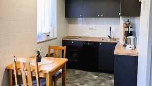 A compact kitchen with dark cabinets, a wooden dining table, and a single chair. - Vacation apartment 1 - Ferienhof Rätzsee (Wustrow)