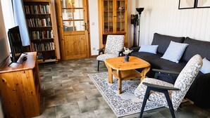 A cozy living room with a dark sofa, patterned armchairs, a wooden coffee table, and a bookshelf. - Vacation apartment 1 - Ferienhof Rätzsee (Wustrow)