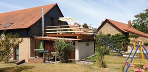 A two-story house with a balcony, outdoor seating area, and a swing set.