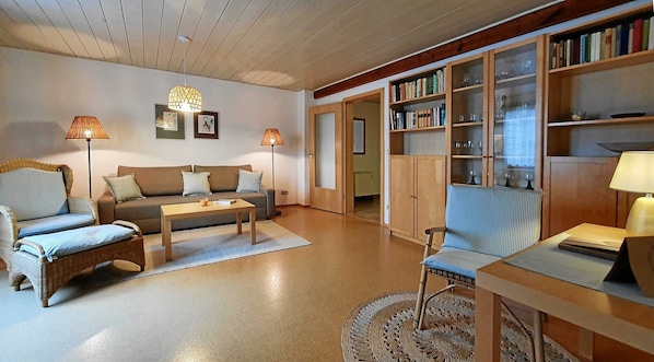 A cozy living room with a sofa, two armchairs, a coffee table, and a bookshelf filled with books.
