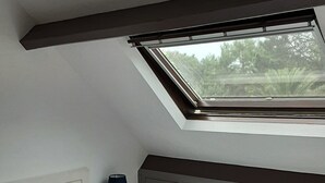 Ein Schlafzimmer mit Oberlicht, einem Bett mit Kissen, einem Nachttisch mit Lampe und einem Kleiderschrank.