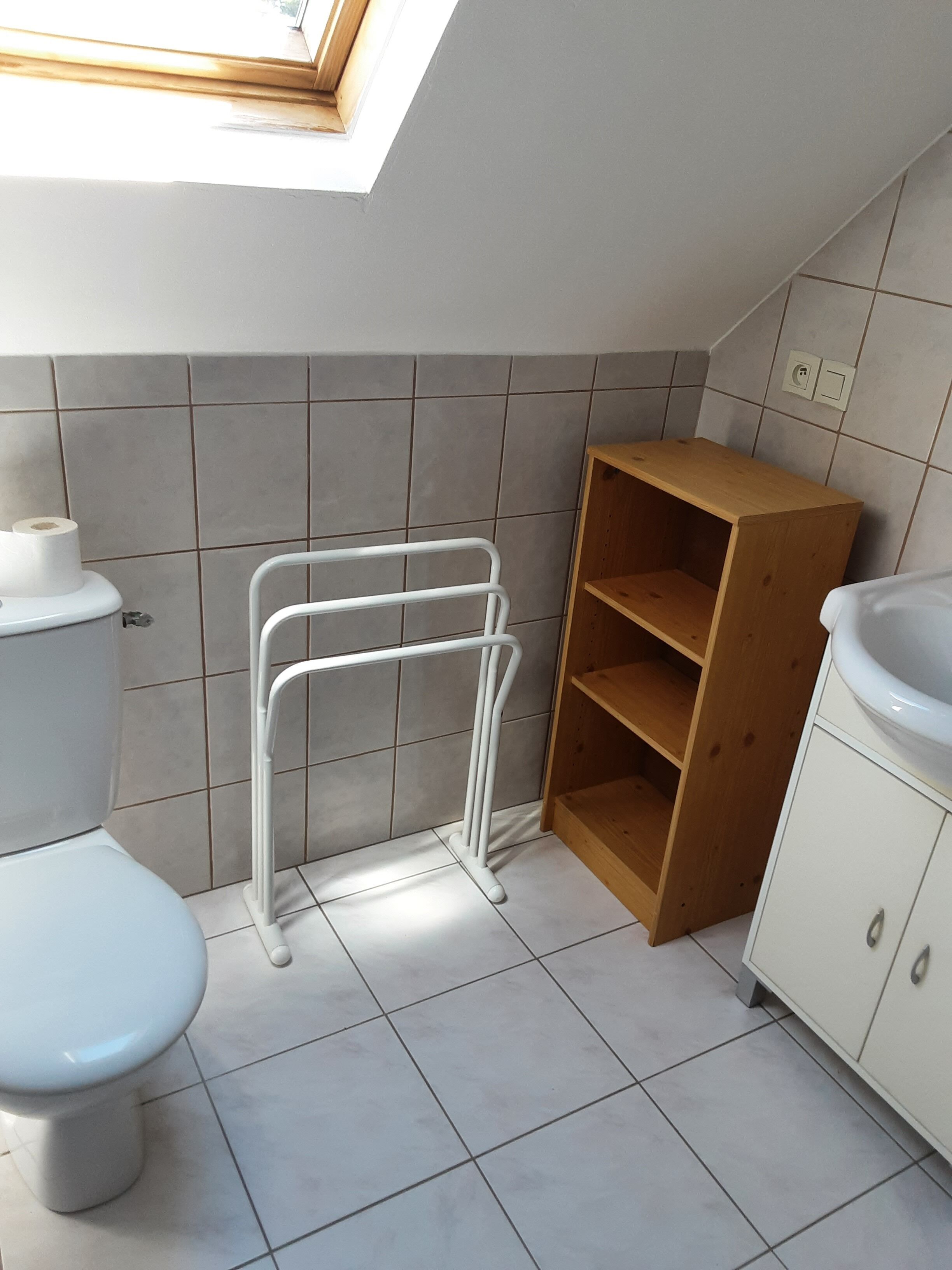 A bathroom with a toilet, a white radiator, a wooden shelf, and a white cabinet.