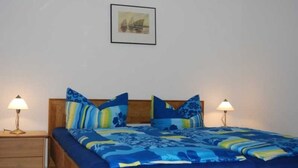 Ein Schlafzimmer mit einem hölzernen Bett, blau-gelber Bettwäsche mit Muster, zwei Nachttischlampen und einem gerahmten Bild an der Wand.